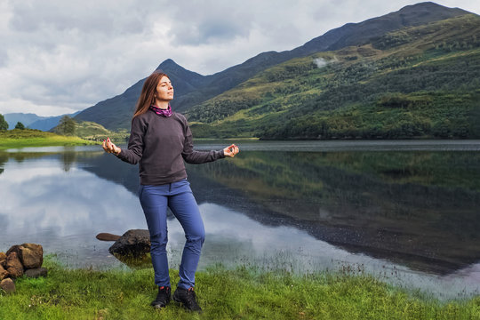 Young woman tourist standing near the wery calm and peaceful lake with her eyes closed enjoying the nature