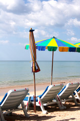 Colorful umbrellas and deck chairs near the sea with clouds above on Phuket island beach  