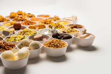 Rangoli of sweets and Farsan/snacks in bowls for Diwali with diya over white background