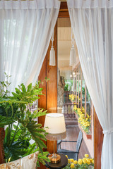 Vintage home interior with lamp on table and white curtain under wooden and glass window decorated with marigold flower.