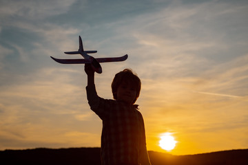 Little boy aviator over sunset. Little children with toy airplane in a field at sunset. Success and child leader concept.