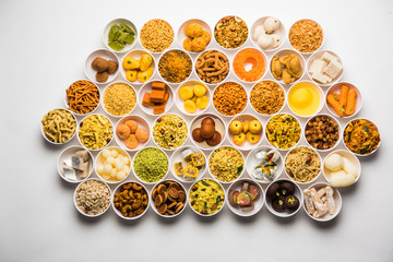 Rangoli of sweets and Farsan/snacks in bowls for Diwali with diya over white background