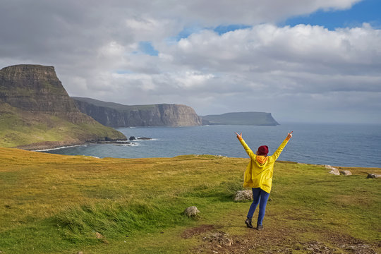 Woman traveller standing with her hends raised on the beautiful scenic coast