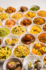 Rangoli of sweets and Farsan/snacks in bowls for Diwali with diya over white background