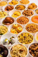 Rangoli of sweets and Farsan/snacks in bowls for Diwali with diya over white background
