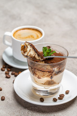 Portion of Classic tiramisu dessert in a glass and cup of coffee on concrete background