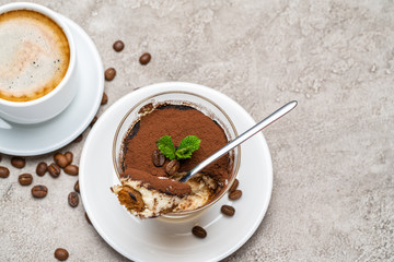 Portion of Classic tiramisu dessert in a glass and cup of coffee on concrete background
