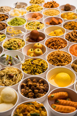 Rangoli of sweets and Farsan/snacks in bowls for Diwali with diya over white background