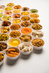 Rangoli of sweets and Farsan/snacks in bowls for Diwali with diya over white background