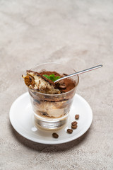 Portion of Classic tiramisu dessert in a glass cup on concrete background