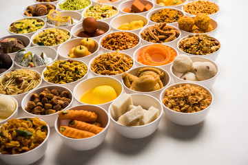 Rangoli of sweets and Farsan/snacks in bowls for Diwali with diya over white background
