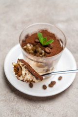 Portion of Classic tiramisu dessert in a glass cup on concrete background
