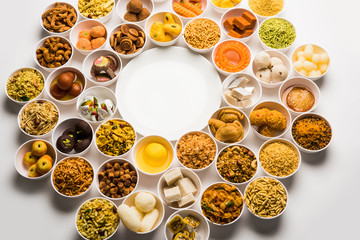 Rangoli of sweets and Farsan/snacks in bowls for Diwali with diya over white background