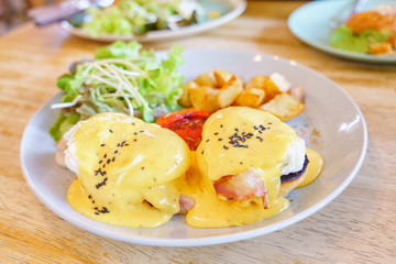 Close up egg benedict with organic salad and fried potato on with dish on wooden table background. delicious breakfast in morning..