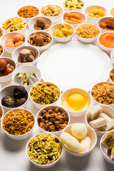 Rangoli of sweets and Farsan/snacks in bowls for Diwali with diya over white background