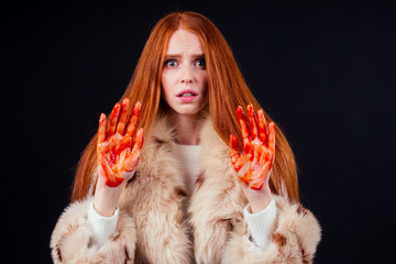sad redhaired ginger fashion victim woman with blood on her hands wearing natural fur coat and...