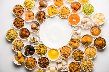 Obraz na płótnie Canvas Rangoli of sweets and Farsan/snacks in bowls for Diwali with diya over white background