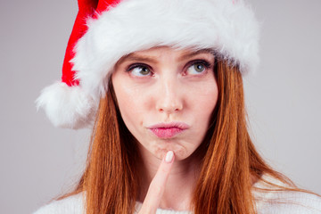 thoughtful beautiful redhaired ginger woman wearing white knitted sweater and santa claus hat...