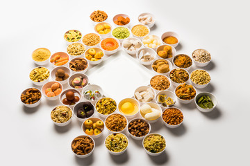 Rangoli of sweets and Farsan/snacks in bowls for Diwali with diya over white background