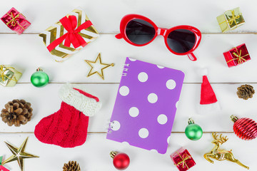 Christmas New year theme object (gift box ,Santa sock, sun glasses, violet notebook, star, pine cone, reindeer, Santa hat) decorated on white wooden table desk and background.Holiday festival concept.