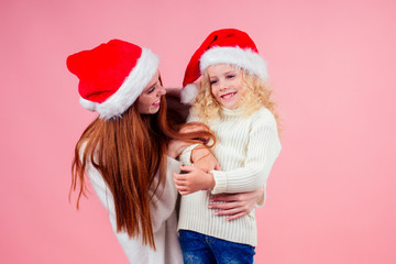 ,happy redhead ginger woman and cute little blonde girl wearing santa claus hat and having fun together in studio pink background