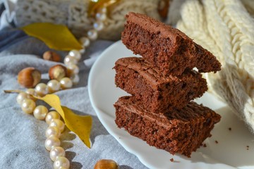 Chocolate brownie cake on a white plate with hazelnuts and autumn leaves on background.