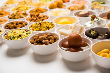Rangoli of sweets and Farsan/snacks in bowls for Diwali with diya over white background