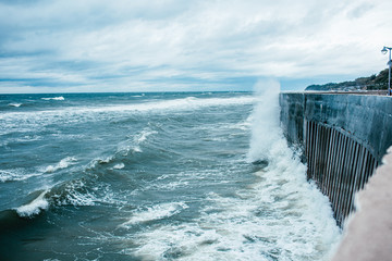 Scary Stormy Waves with Big Sea Wave Splashing Over pier Road at cloudy autumn rainy day. High wave is breaking on the pier