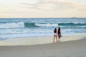 Madre e hija caminado en la playa en el atardecer