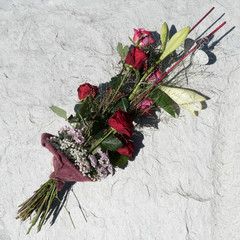 Beautiful arranged floral bouquet in a violet sleeve placed on a stony background. Flower bouquet with Red Naomi roses, Lilium Longiflorum, Gypsophila, Chrysanthemum Santini and Deep Purple roses.