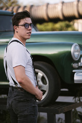 Fototapeta na wymiar Guy in a shirt with suspenders posing at the retro car