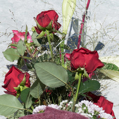 Beautiful arranged flower bouquet in a violet sleeve on a stone. In the background there is a white heart as a decoration visible.