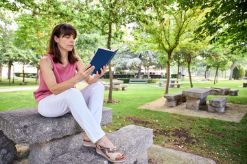 woman reading a book outdoors in a park