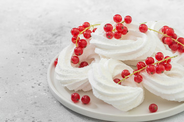 Meringues in the form of rings with bunches of red currants on a white plate