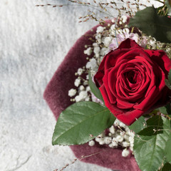One Red Naomi rose arranged with green leaves, grasses, chrysanthemum santini and gypsophila in a violet sleeve. Copy space in the stony background.
