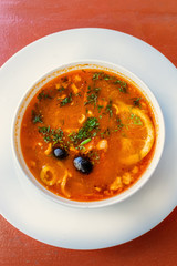 Russian red soup Solyanka, with sausage, olives and lemon. top view on the red table. close up vertical