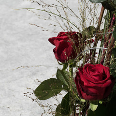 Detail of two Red Naomi roses with green leaves and grasses in a bouquet on one half of the image and copy space on the other half.