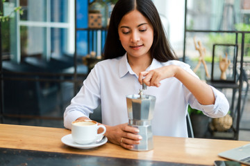 Asian woman drinking coffee with coffee grinder in cafe