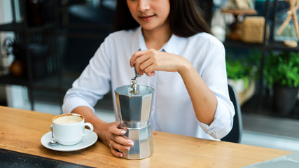 Asian woman drinking coffee with coffee grinder in cafe