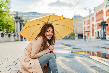 Happy young woman standing under umbrella in rain, laughing. Joyful woman walking in rainy weather. I love it when it's raining! Beautiful woman with umbrella on a rainy day.