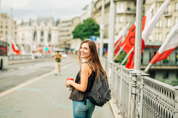 Outdoor portrait of beautiful young woman in the city, wearing backpack, holding cup of take away...