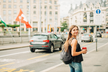 Outdoor portrait of beautiful young woman walking down the road in the city, wearing backpack,...