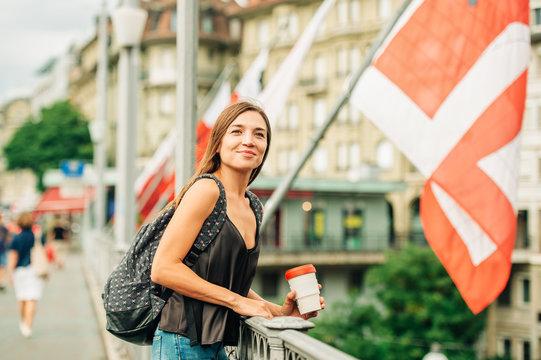 Outdoor portrait of beautiful young woman in the city, wearing backpack, holding cup of take away coffee. Image taken in Lausanne downtown, place Bel Air, Switzerland