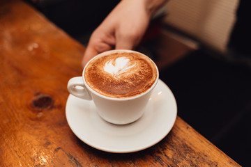 Hand barista holding and serving cup of coffee.