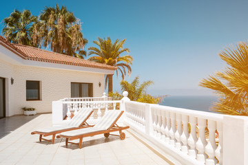 sunny terrace with sun beds of ocean view house with palm trees anb blue sky copy space