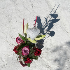 Beautiful arranged floral bouquet with Red Naomi and Deep Purple roses on a stony background. Purple sleeve around the flowers at the bottom and on the top of the bouquet a white heart as decoration.