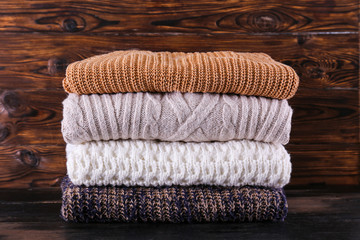 Obraz na płótnie Canvas Bunch of knitted pastel color sweaters with different knitting patterns perfectly folded in stack on brown wooden table, wood textured background. Fall winter season knitwear. Close up, copy space.