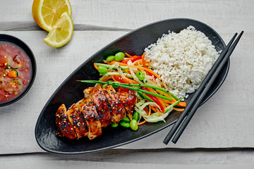 Traditional Japanese teriyaki chicken with salad made of cucumber, ginger, carrot, pepper and cabbage, rice, sesame and edamame with lemon and sweet chili sauce. Top view, directly above.