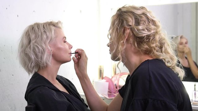 Visagist making a professional make up for a beautiful blonde young woman model before a photo session.