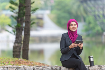 Obraz premium Muslim Businesswoman with her tablet and her coffee at the park.
